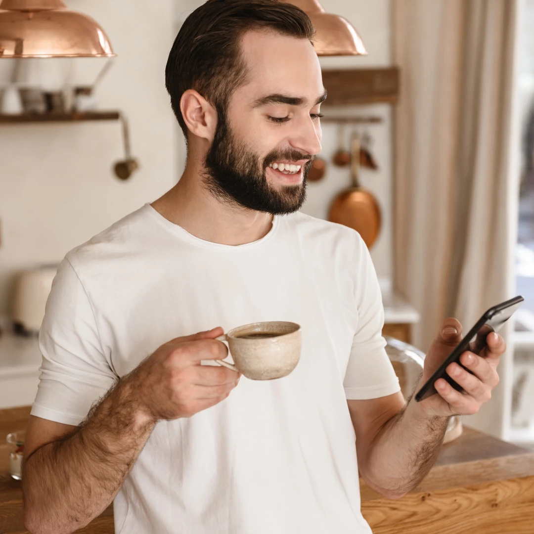 Smilende mann med kaffekopp ser på mobil