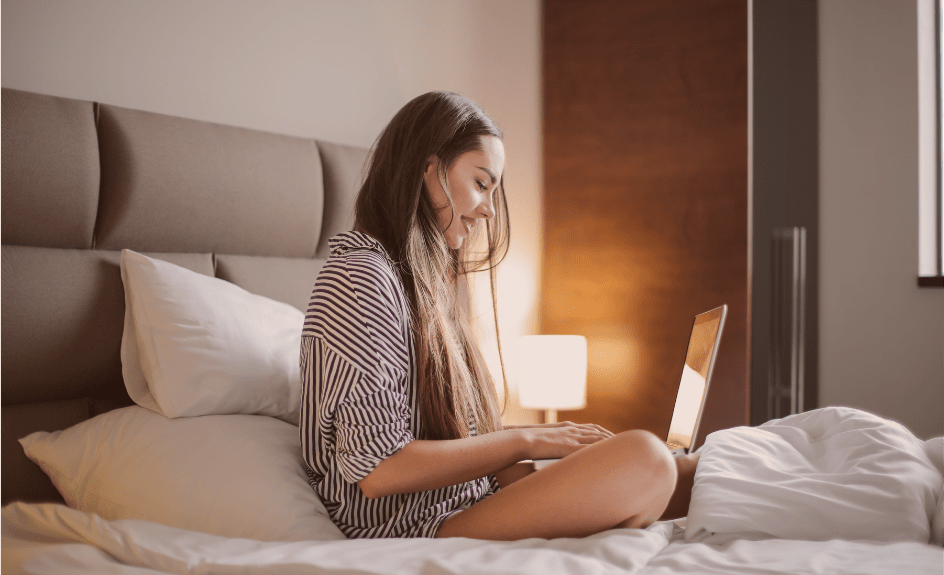 kvinne sitter på seng på hotellrom med pc i fanget