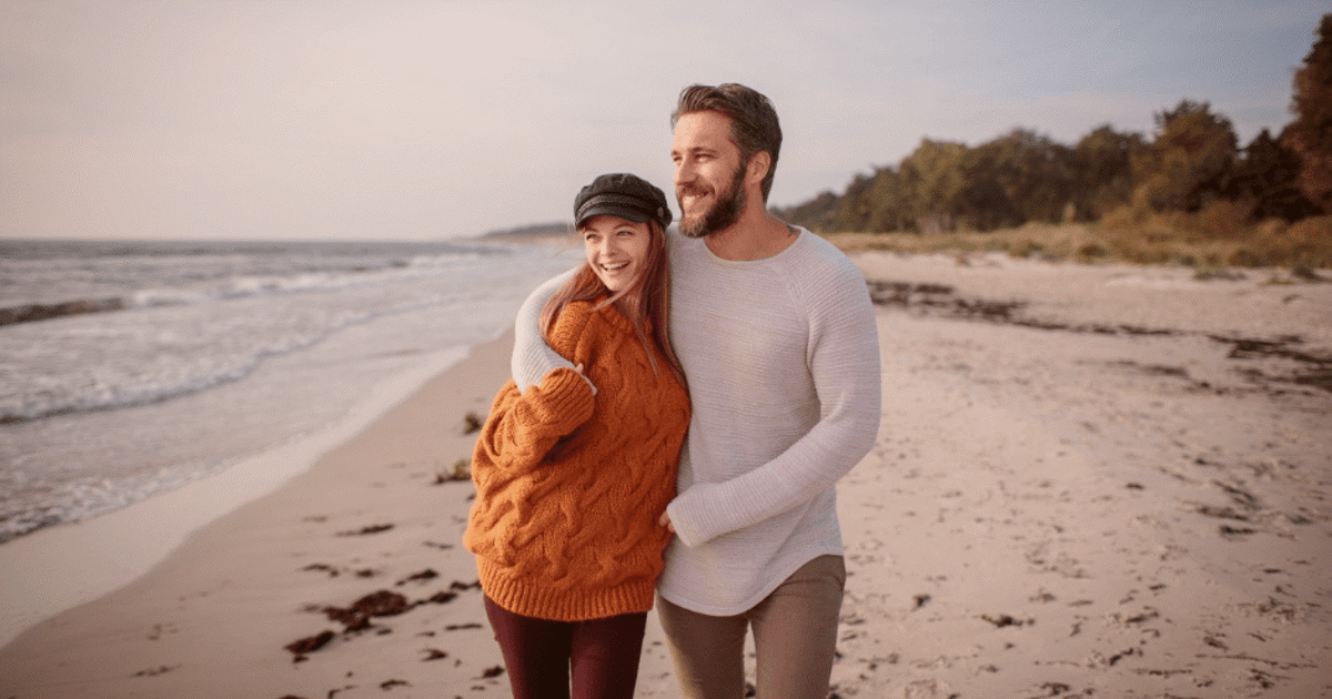Smilende par går på strand på ferie