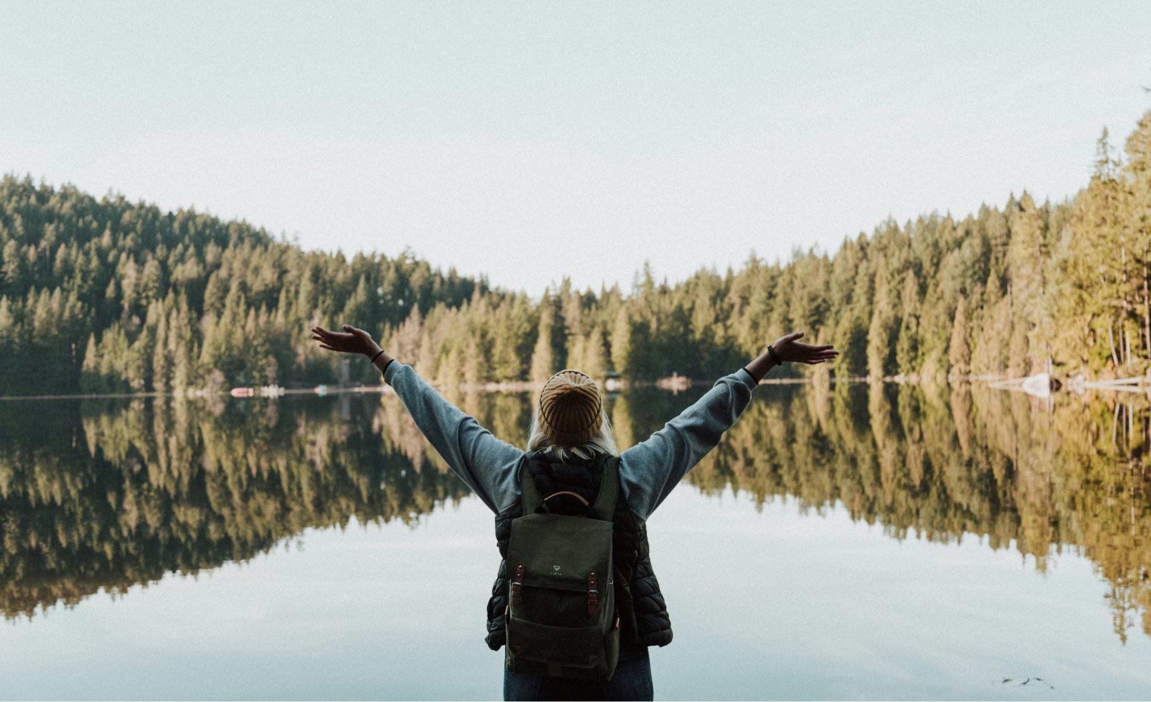 Fri kvinne ute på tur ser over innsjø i skog