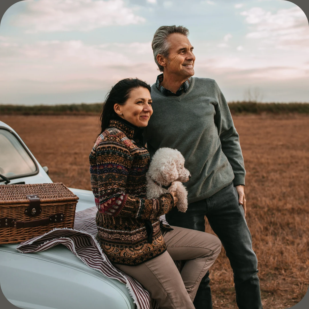 Smilende eldre par med hund sitter på bil